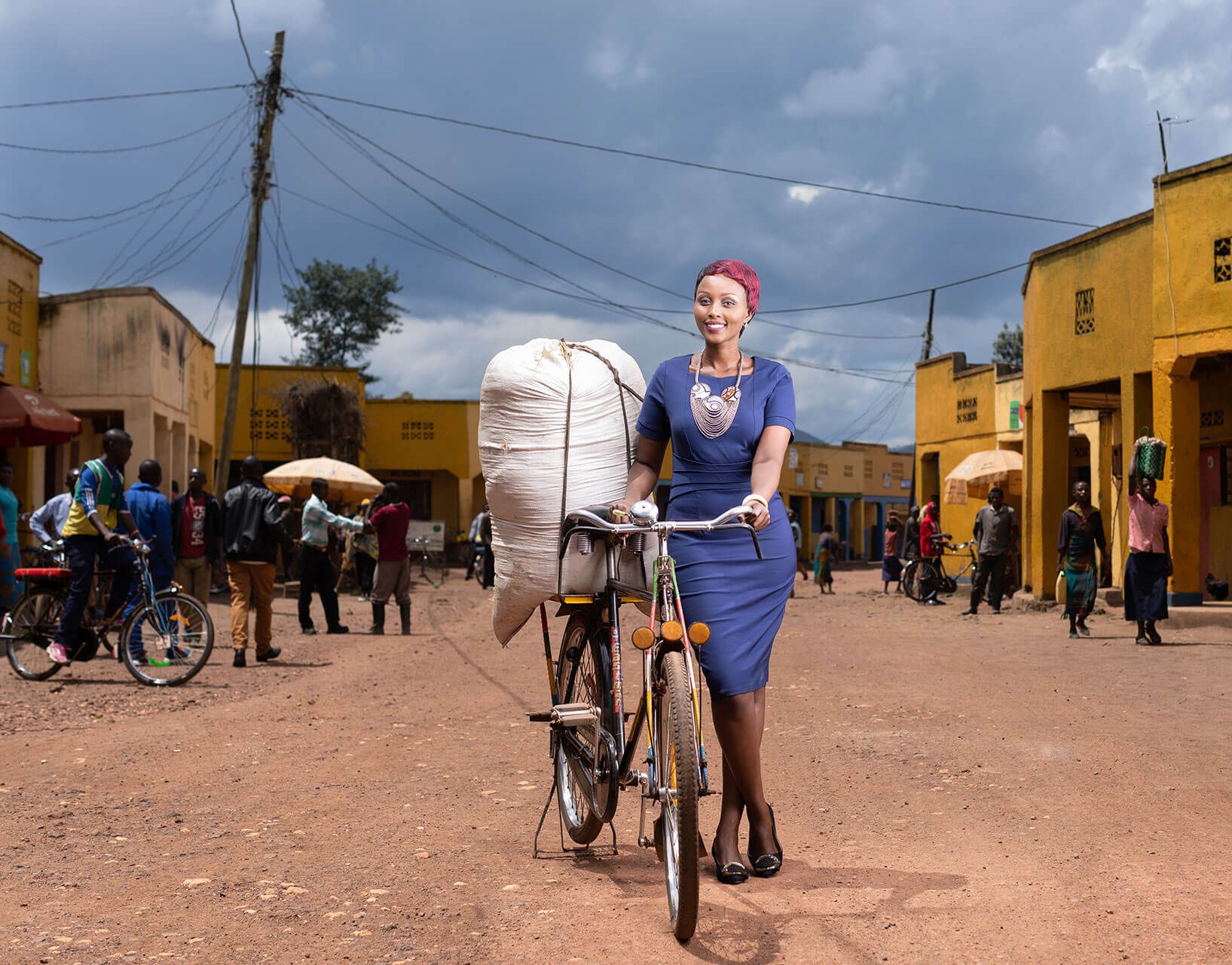 A woman walking her bicycle towards iCRA surrounded by agricultural fields, symbolizing resilience and rural community development