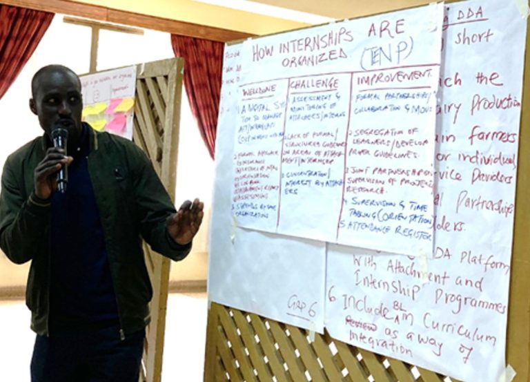 Man talking into a microphone gesturing towards flipcharts on the wall with content about internship organisation